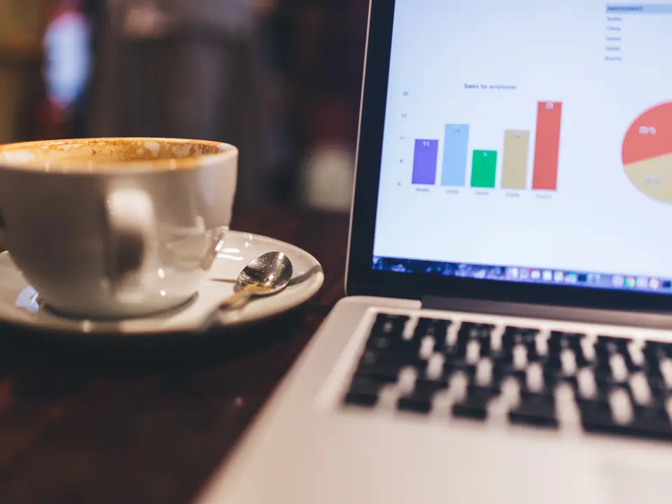 Xícara de café ao lado de um notebook com um gráfico de barras na tela